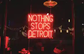 Neon sign reading "Nothing Stops Detroit" glowing in a cozy bar window at night.